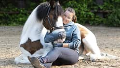 Michelle Menger sitzt mit ihrem Pony Joschi im Sand zum Kuscheln
