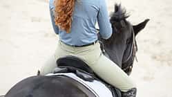 Eine Reiterin von hinten mit Fokus auf dem Hintern im Sattel.