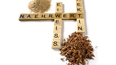 Buchstaben, die in Scrabble-Manier gelegt wurden und die Worte "Nährwert", "Eiweiss" sowie "Pektin" bilden. Drumherum sid kleine Häufchen Pferdefutter drapiert.