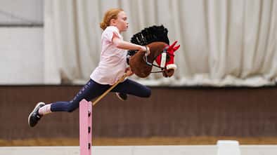 Ein Mädchen zu den UK Hobby Horse Championships 2024 mit einem braunen Steckenpferd über dem Sprung