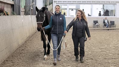 CAVALLO Boden-Dressur, Nadine Szymanski führt Pferd in Halle mit Trainerin Claudia Münch, beide von vorn