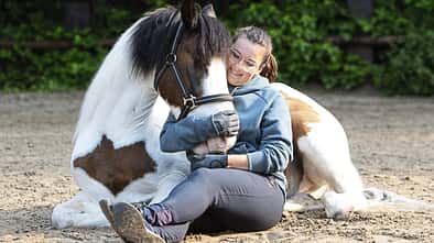 Michelle Menger sitzt mit ihrem Pony Joschi im Sand zum Kuscheln