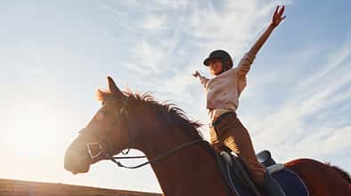 Wundreiten, Gelände, Sonnenuntergang, Freude beim Reiten Ein junges Mädchen stellt sich in die Bügel auf ihrem Pferd bei Sonnenuntergang im Gelände