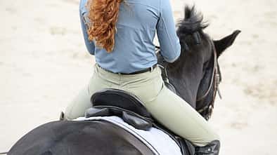 Eine Reiterin von hinten mit Fokus auf dem Hintern im Sattel.