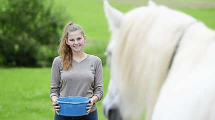 Ein Mädchen mit Futterschüssel in der Hand steht vor ihrem Pferd