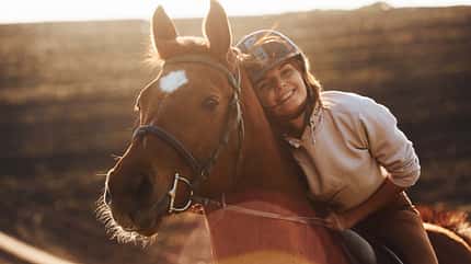 Eine junge Frau mit ihrem Pferd bei sonnigem Wetter auf dem Feldweg.