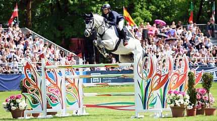 Michi Jung über dem Sprung mit Schimmel zum Pferd International München