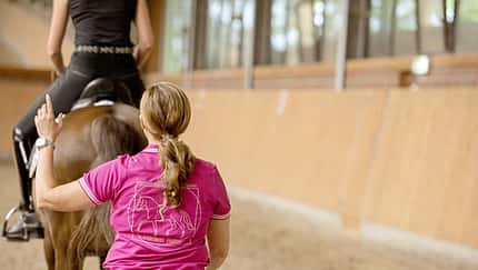 CAVALLO Biomechanisch richtiger Reitersitz, Trainierin Daniela Rahn schaut von hinten auf den korrekten Sitz der Reiterin in Reithalle
