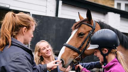 Mother and instructor preparing young girl for horseback riding lesson Mother and instructor preparing young girl for horseback riding lesson