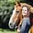 Reiterin, Pferd, Pferdeporträt, Reitsport, Mensch-Tier-Interaktion, Tierfotografie, Outdoor-Porträt, Naturhintergrund, Blesse Das Foto zeigt eine Frau in Nahaufnahme neben einem fuchsfarbenen Pferd mit breiter weißer Blesse; sie hält den Kopf des Tieres und blickt lächelnd in die Kamera. Es handelt sich um ein Outdoor‑Porträt mit geringer Tiefenschärfe vor einem grünen, unscharfen Naturhintergrund. Die Komposition betont die Nähe zwischen Mensch und Tier.