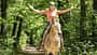 Featherlight Horsemanship, Pferdetraining, Geländereiten, Reithelm, Waldweg, Niederlande, Horsemanship, Freizeitreiten, Reiterin, Pferd, Yvette Blokesch Das Foto zeigt eine Reiterin mit Reithelm auf einem Pferd beim Ausritt auf einem schattigen Waldweg, die Arme seitlich ausgestreckt.