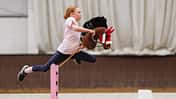 Ein Mädchen zu den UK Hobby Horse Championships 2024 mit einem braunen Steckenpferd über dem Sprung