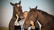 Pferd kuscheln, schmusen, besondere Freundschaft zwischen Mensch und Pferd, Vertrauen, Pferdeliebe Ältere blonde Frau hält links und rechts zwei braune Pferde im Arm und kuschelt mit ihnen.