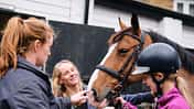 Mother and instructor preparing young girl for horseback riding lesson