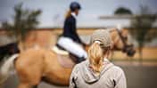 Eine Frau von hinten mit Blick in Richtung einer Turnierreiterin auf dem Abreiteplatz
