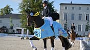 Vorjahressiegerin Dominique Filion (NED) mit ihrem Pferd The Boss, welcher eine hellblaue Paradedecke trägt, zur Ehrenrunde beim Neustädter Pferdesommer 2025.