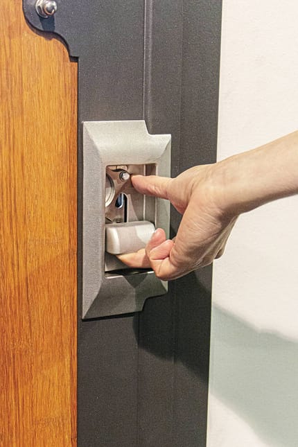Türverschluss, Einlassgriff, Riegelmechanismus, Sicherheitsverriegelung, Türbeschlag, Metallrahmen, Handbedienung, Detailaufnahme, Industriegriff, Innenmechanik Die Nahaufnahme zeigt einen Außenboxen-Verschluss von Röwer & Rüb. Er verfügt über einen neuen Griff mit kleiner Edelstahlschale. Eine Hand betätigt den Mechanismus.